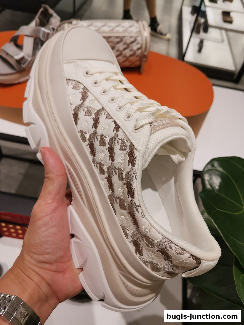 A hand holds a stylish white sneaker with a patterned fabric and a thick sole.