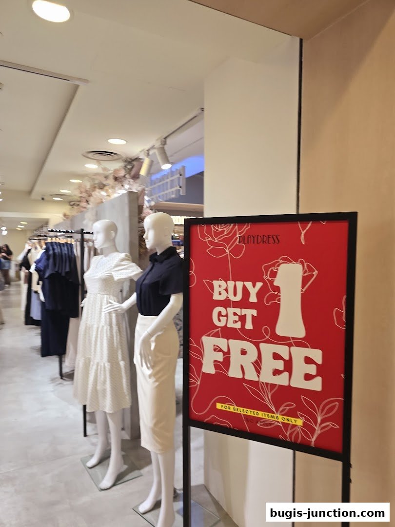 Mannequins display dresses inside a clothing store with a 'Buy 1 Get 1 Free' sign.