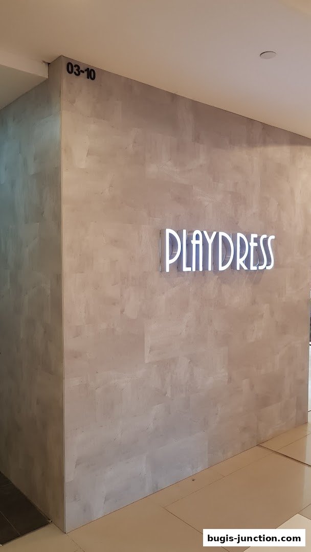 The Playdress store sign is illuminated on a textured wall with unit number 03-10.