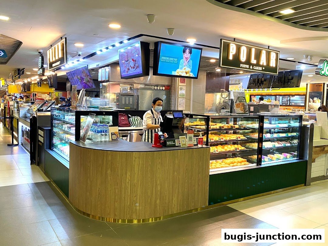 A brightly lit bakery counter displaying a variety of pastries and cakes, with staff serving customers.