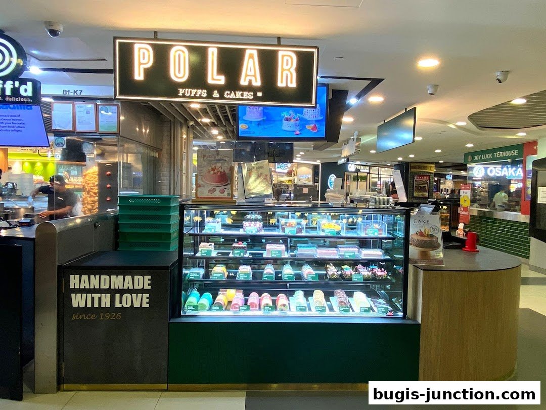 A display of colorful cakes and pastries at Polar Puffs & Cakes, with a "Handmade With Love since 1926" sign.