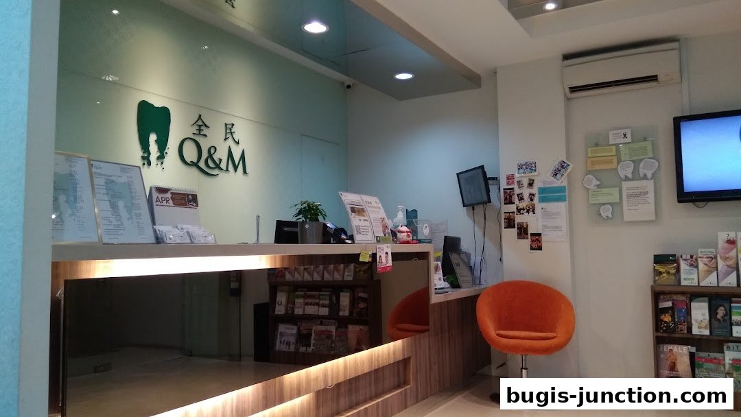 The reception area of Q&M Dental Centre Bugis Junction, featuring a counter, chairs, and dental information.