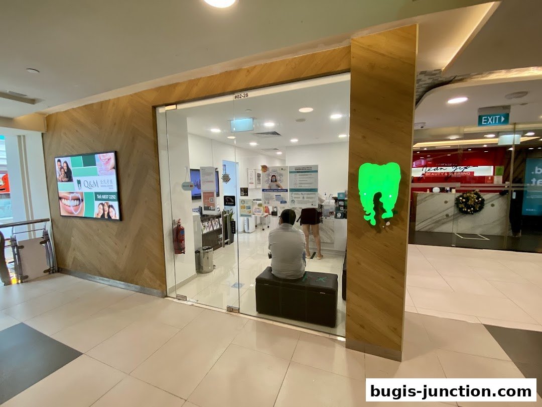 The entrance to Q&M Dental Centre Bugis Junction, featuring a bright green tooth logo and a digital display.