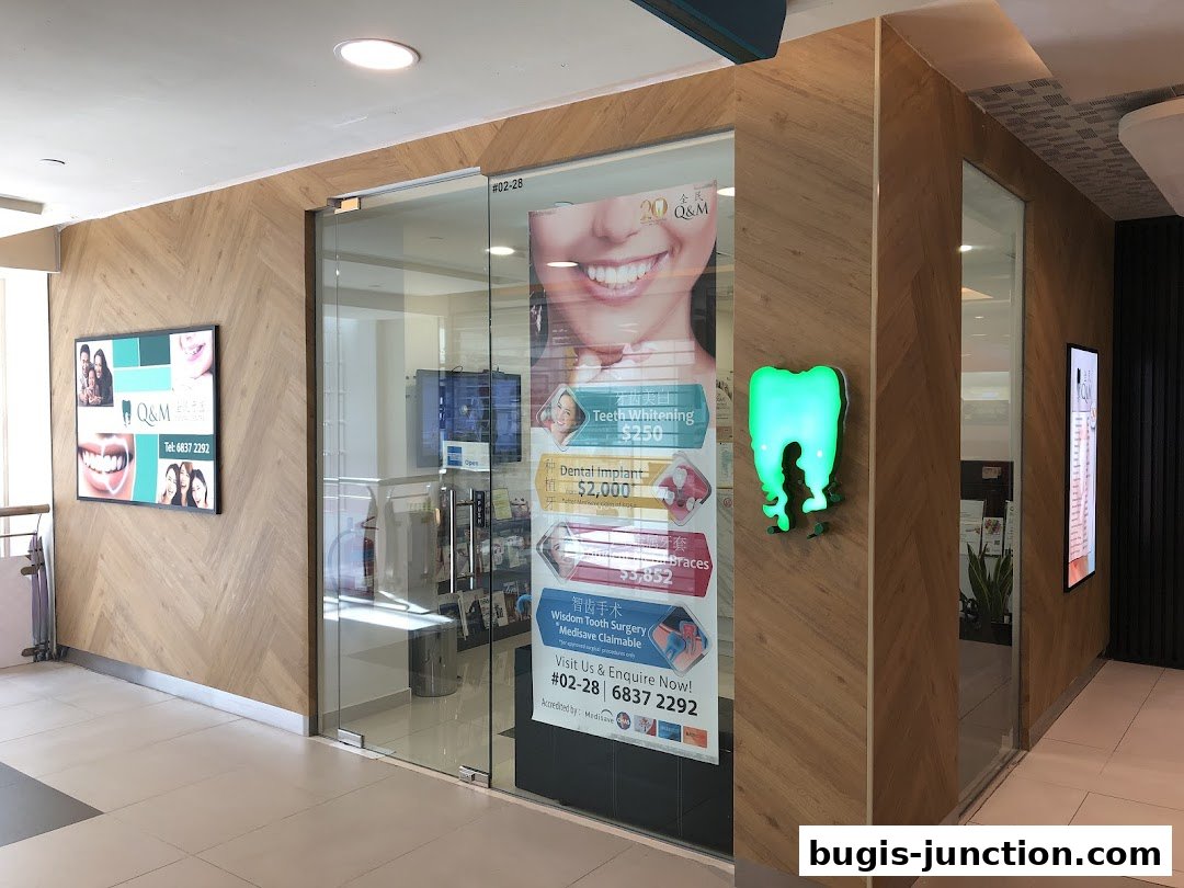 The entrance to Q&M Dental Centre Bugis Junction, featuring promotional posters and a glowing tooth sign.