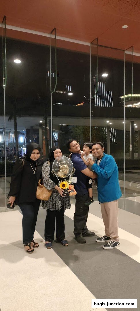 A group of people, including a child, posing for a photo with a balloon and flowers.