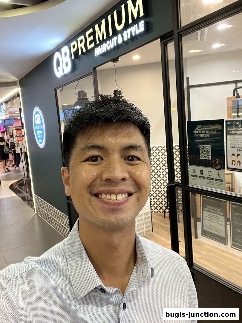 A man smiles in front of the QB PREMIUM Haircut & Style shop.