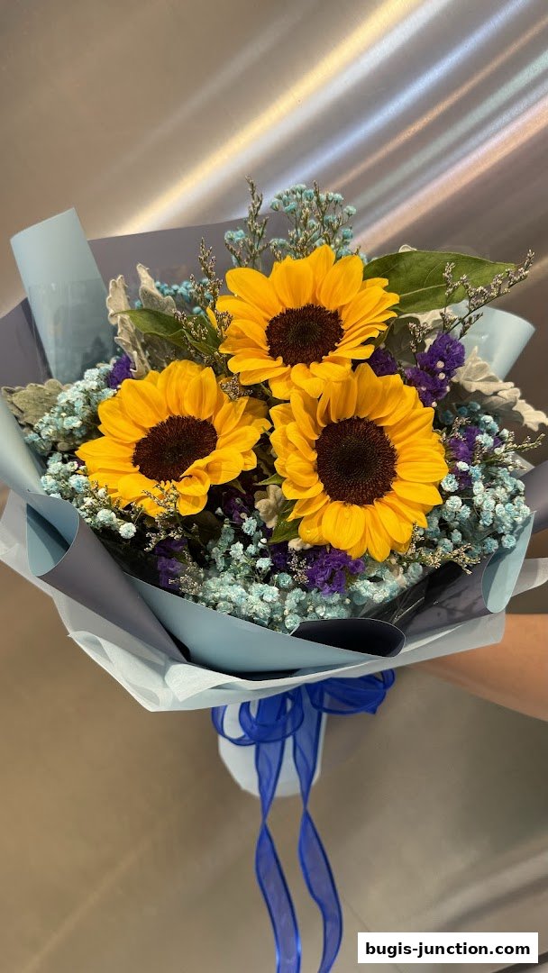 A beautiful bouquet of sunflowers with baby's breath and purple flowers, wrapped in light blue paper.