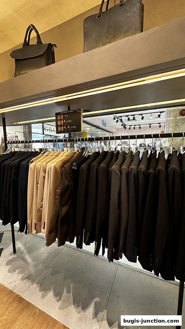 A rack of men's blazers in various neutral colors, with handbags displayed above.