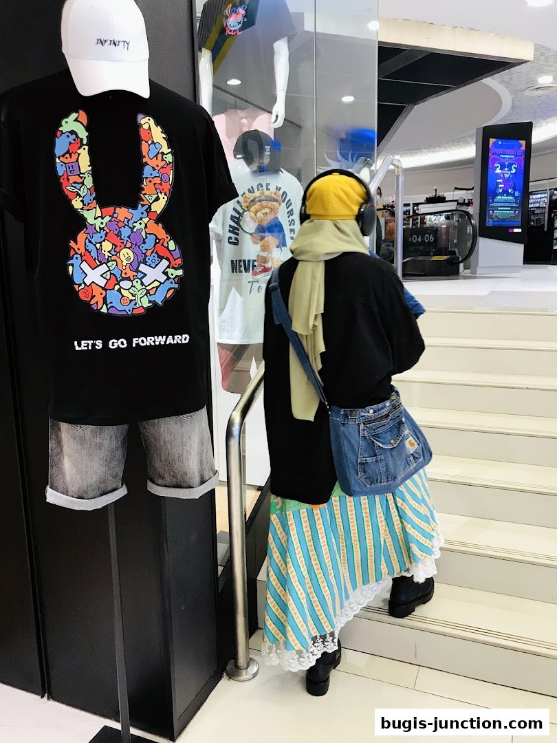 Mannequins display graphic t-shirts and shorts, with a person walking up stairs in the background.