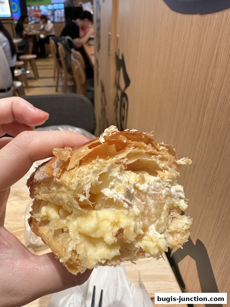 A hand holds a flaky pastry filled with cream and apple filling.