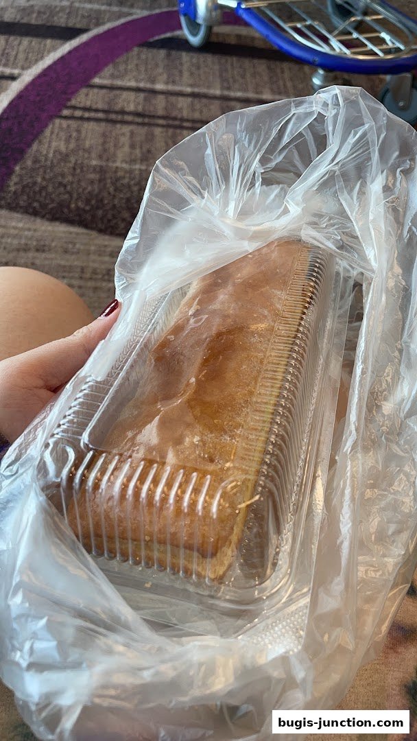 A person holds a plastic bag containing a strudel in a clear plastic container.