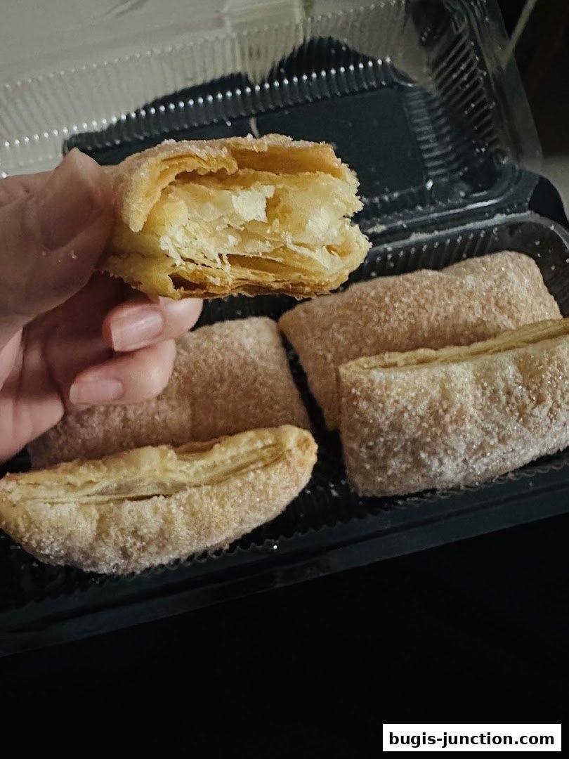 A hand holds a flaky, sugar-dusted apple strudel with a bite taken out.