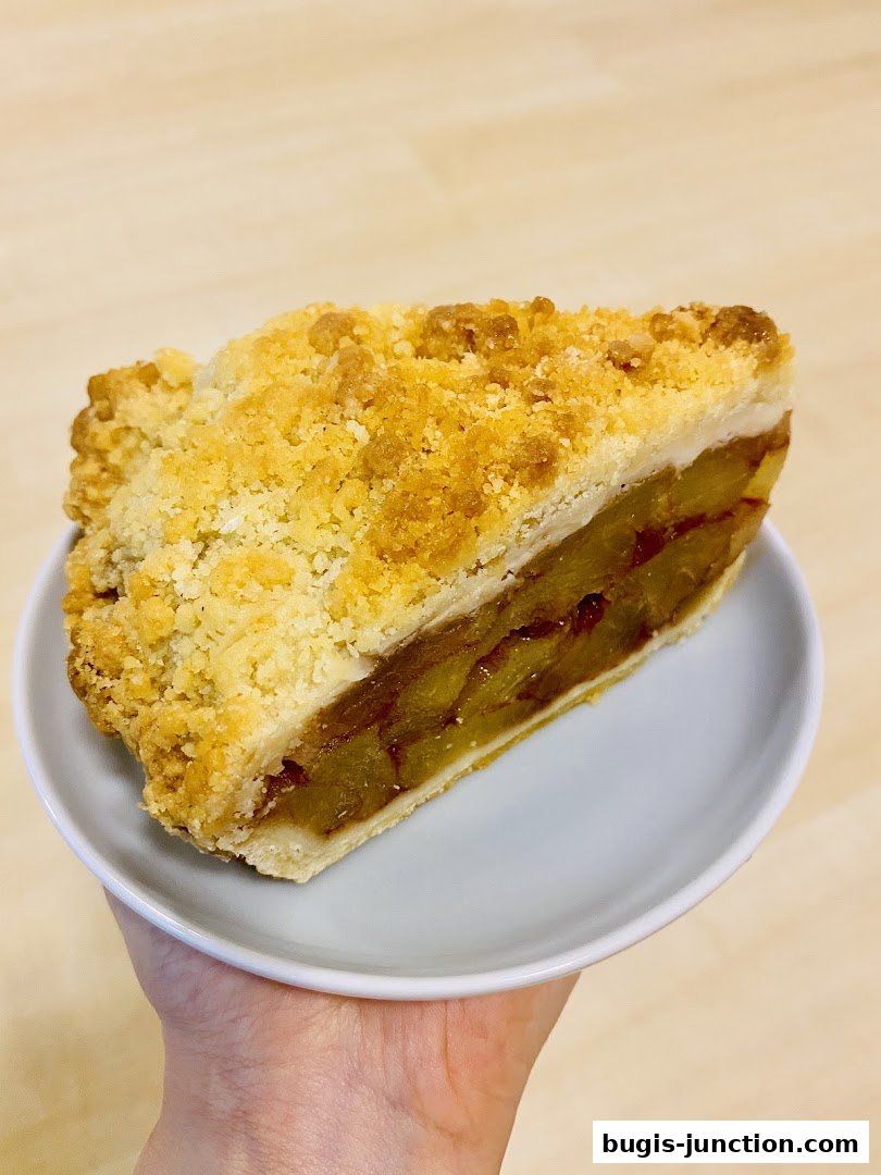 A slice of apple strudel with a crumbly topping on a white plate.