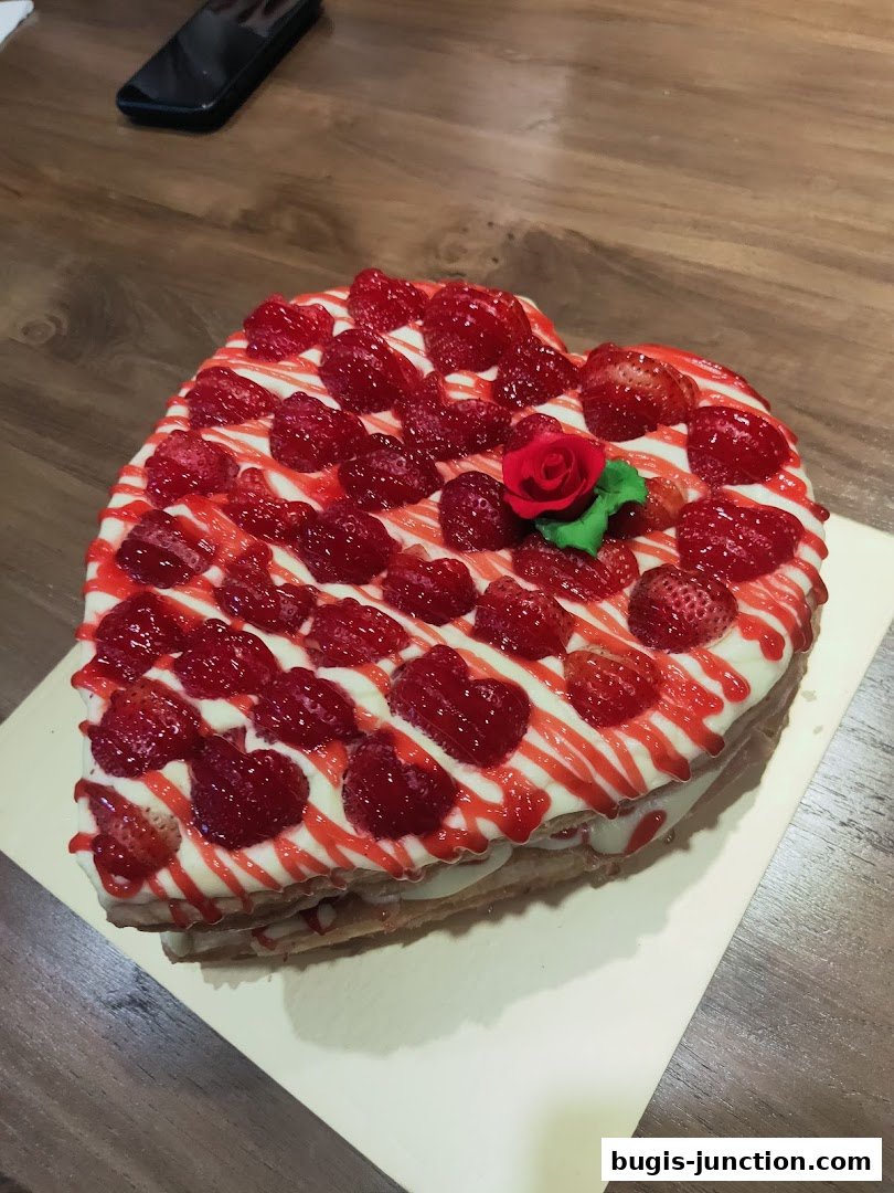 A heart-shaped cake topped with fresh strawberries and drizzled with red sauce.