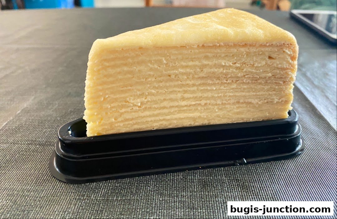 A slice of layered mille-crepe cake with creamy filling, presented on a black stand.