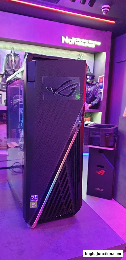 A ROG gaming PC with RGB lighting is displayed in a store with purple ambient lighting.