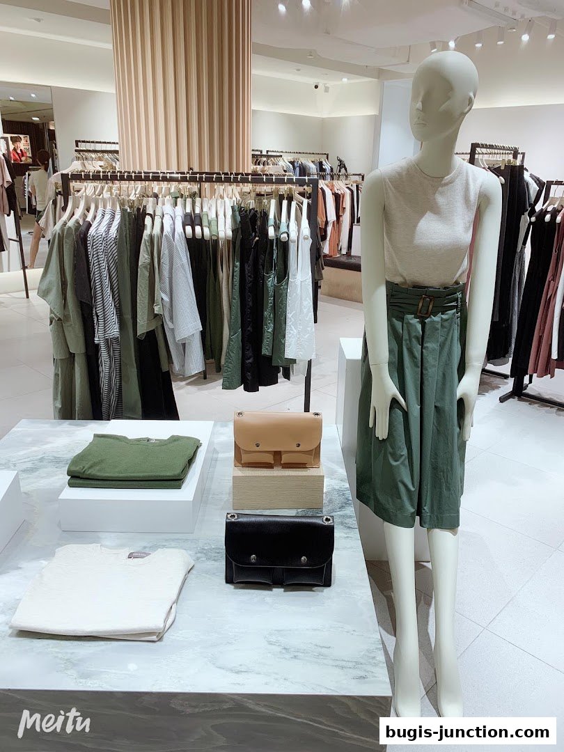 A fashion store interior with clothing racks, a mannequin, and display tables with handbags.
