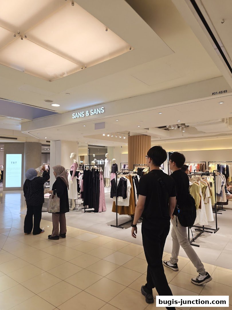People walking past a SANS & SANS clothing store with mannequins and apparel on display.