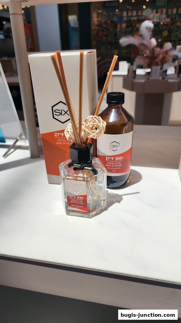 A glass reed diffuser with wooden sticks and decorative balls, next to a bottle and box.