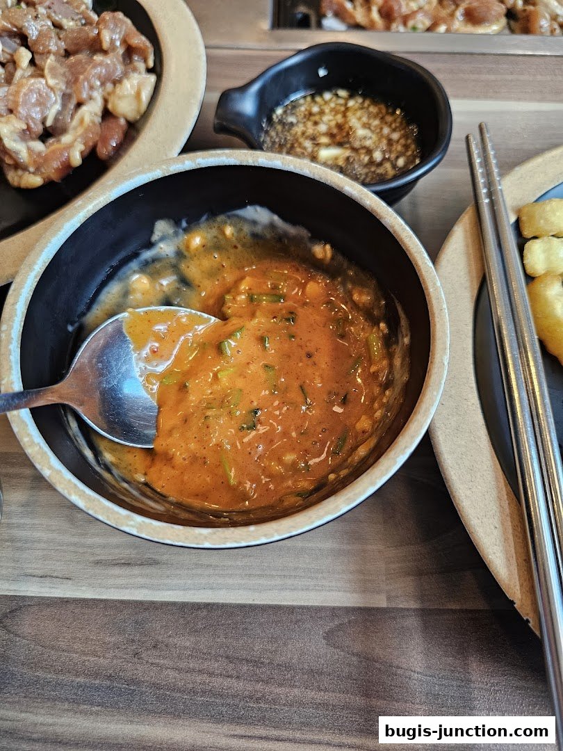 A close-up of a bowl of spicy Korean dipping sauce with a spoon and raw meat.