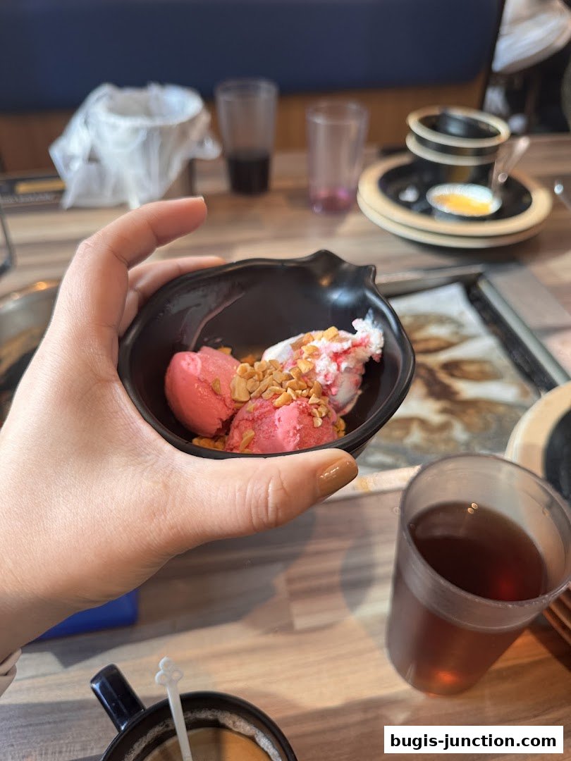 A hand holds a bowl of strawberry ice cream with nuts, next to a glass of iced tea.
