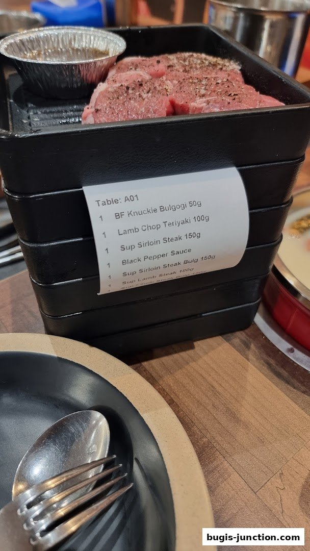 A stack of black trays with raw meat and a sauce, with cutlery on a plate.