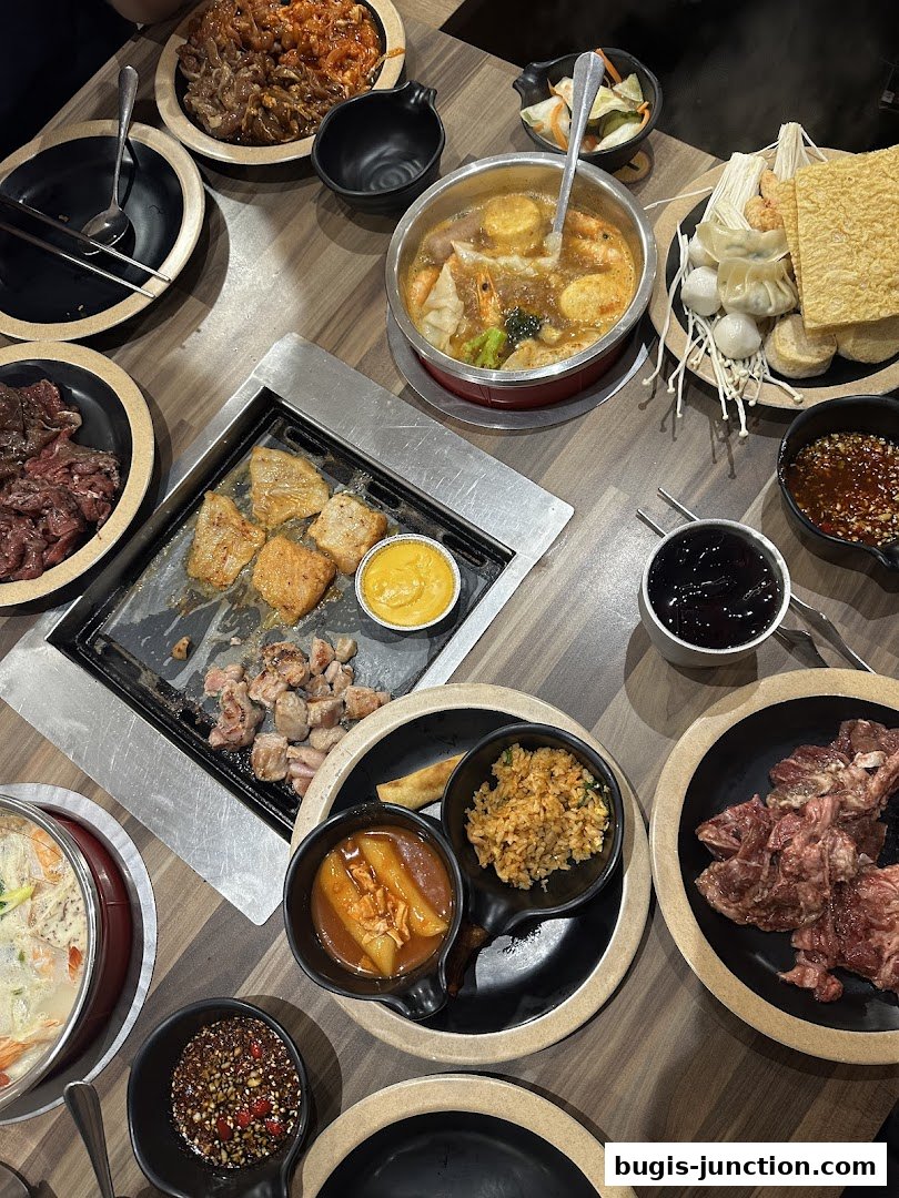 A table laden with Korean BBQ and hot pot dishes, featuring grilled meats, vegetables, and various side dishes.