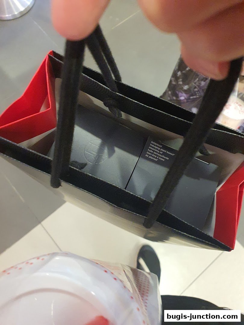 A person holds a Shu Uemura shopping bag with a cleansing oil product inside.