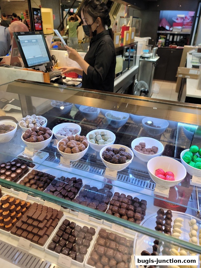A display case filled with various chocolates and a cashier at the counter.