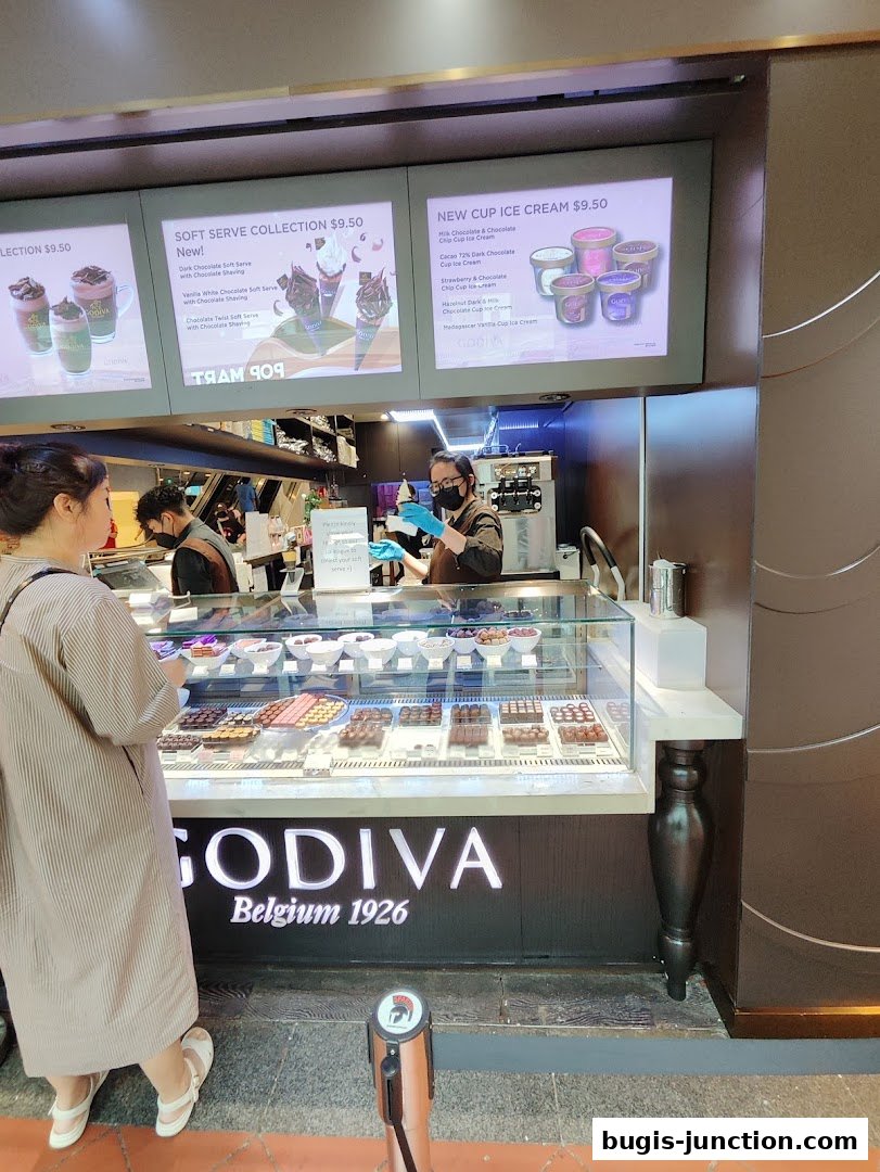 A Godiva chocolate shop counter displaying chocolates and ice cream with promotional screens.
