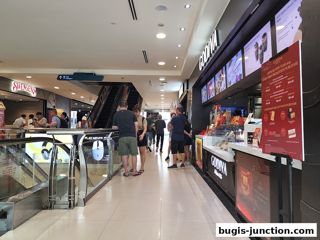A Godiva chocolate shop with customers browsing and a promotional sign.