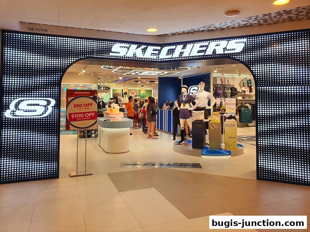 The entrance of a Skechers store with a large illuminated logo and promotional signage.
