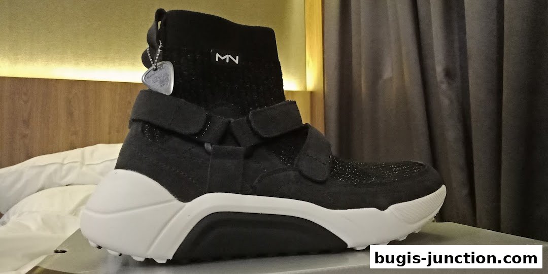 A black Skechers sneaker with white accents and velcro straps is displayed.