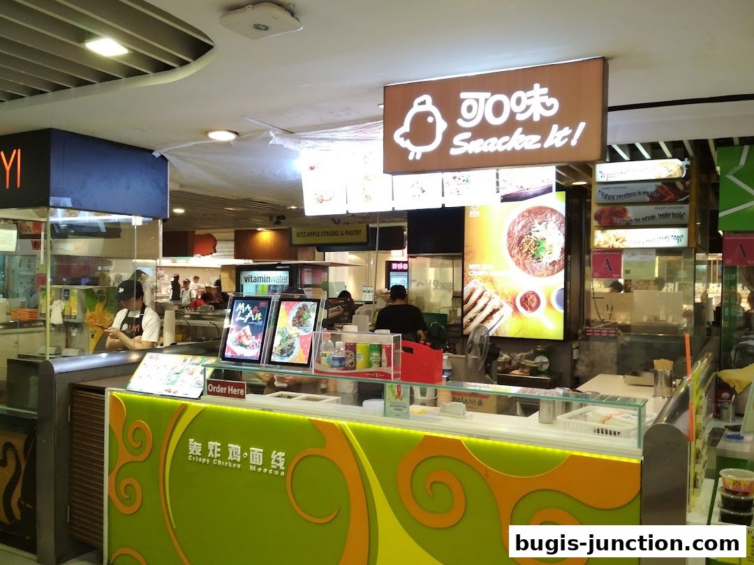 A food stall with a bright sign and display of food items, showing staff preparing orders.
