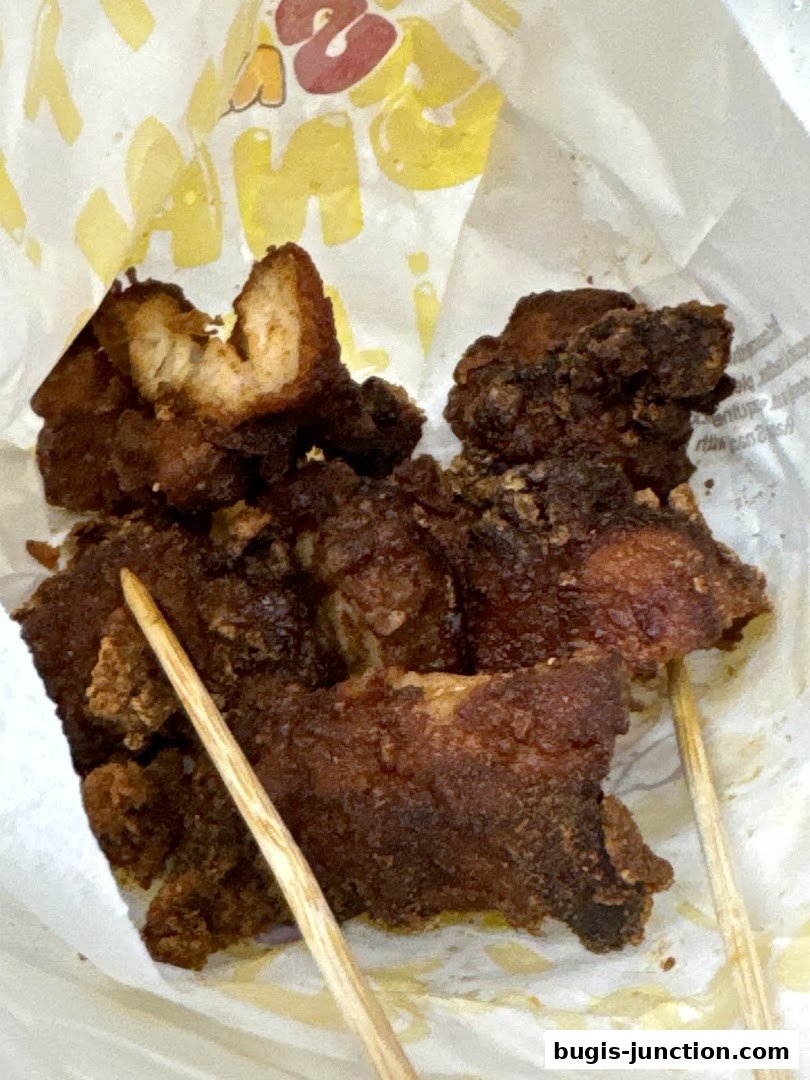 Crispy fried chicken pieces on skewers, served in a paper bag with the shop's logo.