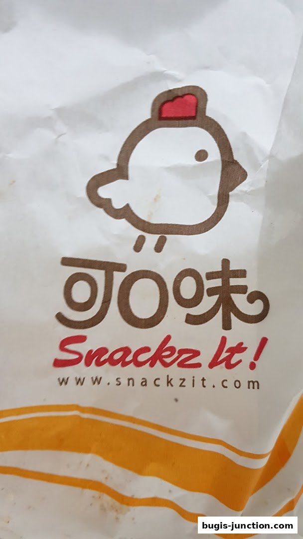 A close-up of a white paper bag with the Snackz It! logo and website.