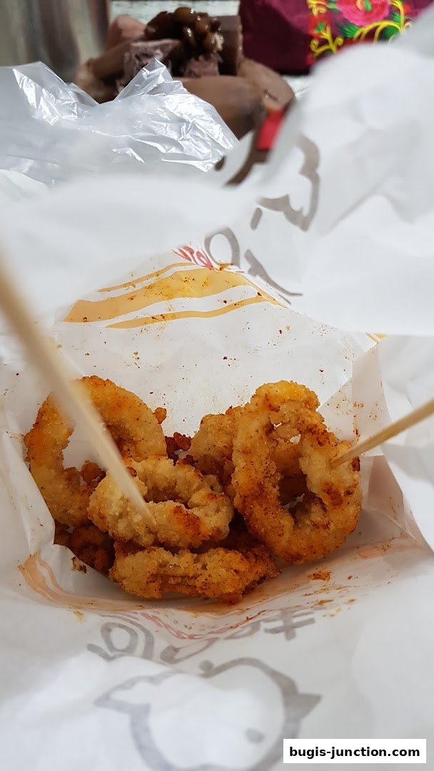 Crispy fried calamari rings seasoned with spices, served in a paper bag with wooden skewers.