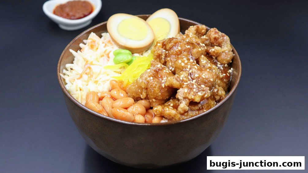 A bowl of savory fried chicken with rice, coleslaw, beans, and a hard-boiled egg.