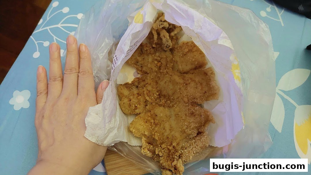 A hand holding a bag of crispy fried chicken pieces.