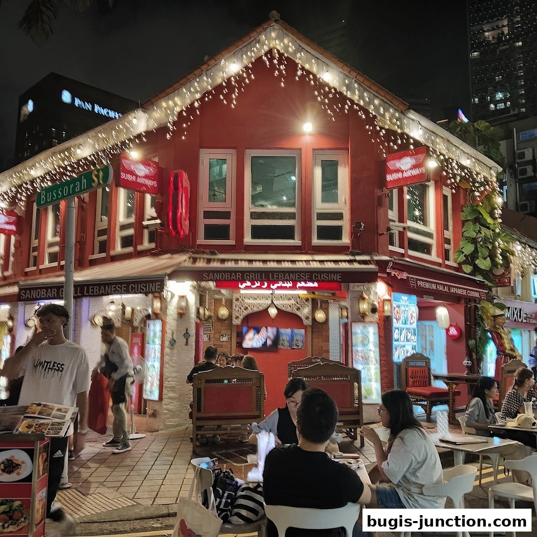 A red building with festive lights, advertising Lebanese and Japanese cuisine, with people dining outside.