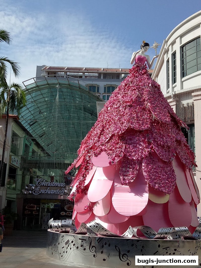 A large pink Christmas-themed decoration with a woman figure on top, set against a building.