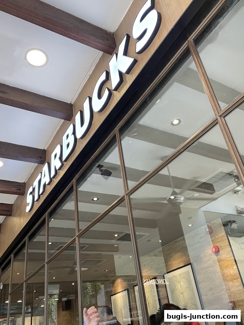 The iconic Starbucks logo illuminated above the shop's glass facade.