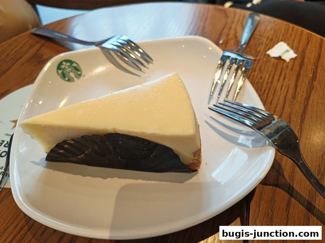 A slice of cheesecake on a white plate with two forks and the Starbucks logo.