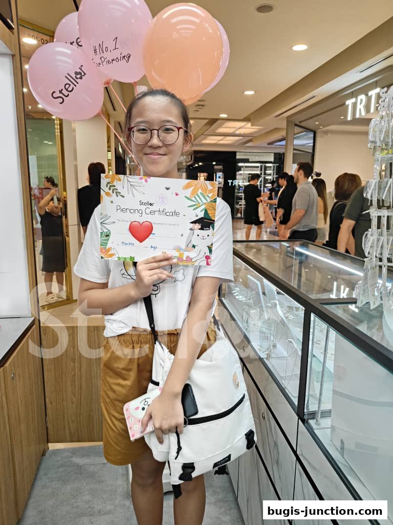 A young girl holds a piercing certificate with balloons from Stellar Ear Piercing.