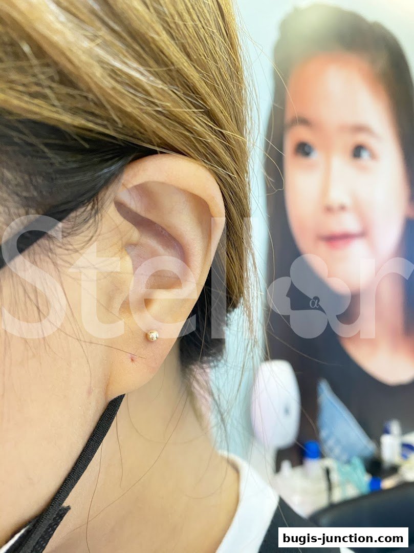 Close-up of a person's ear with a small gold stud earring, with a blurred image of a child in the background.