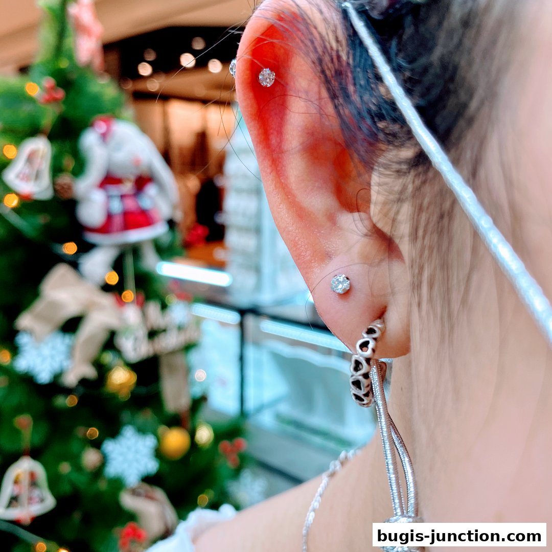 Close-up of a person's ear with multiple piercings and jewelry, with a blurred Christmas tree in the background.