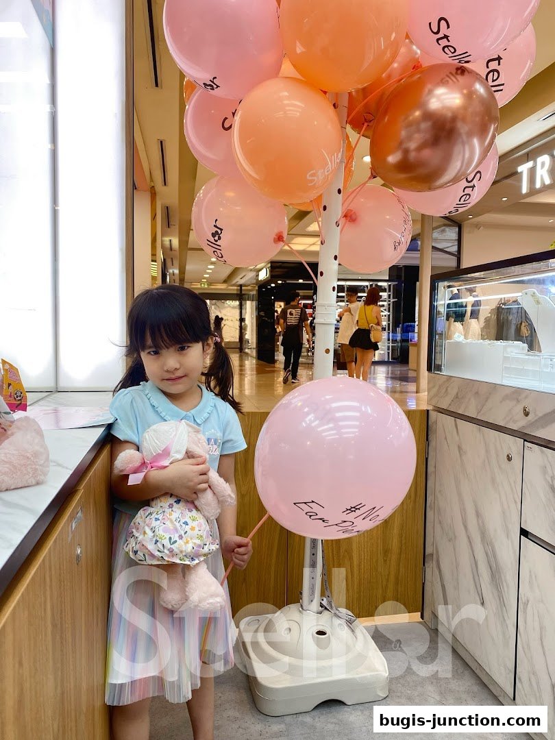 A young girl holds a stuffed bunny in front of balloons at a jewelry store.