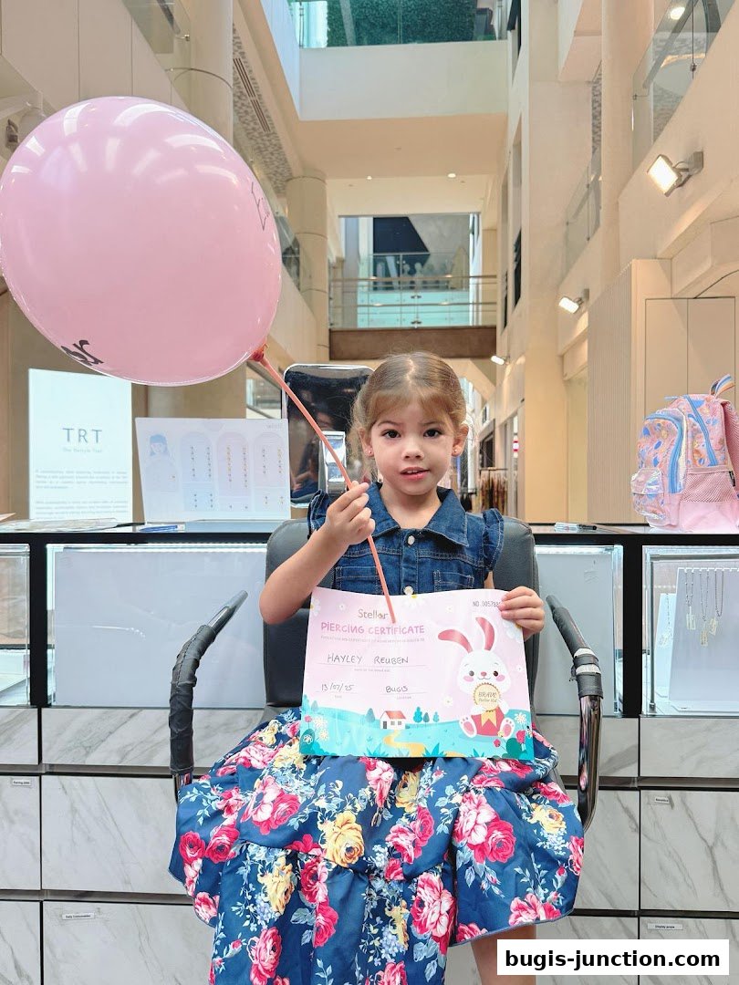 A young girl holds a piercing certificate and a pink balloon in a jewelry store.