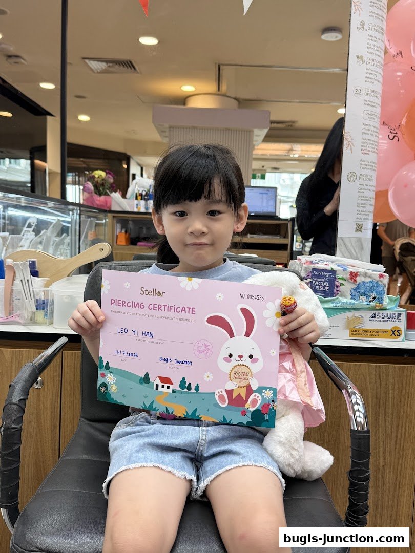 A young girl proudly holds a piercing certificate and a lollipop after her ear piercing.