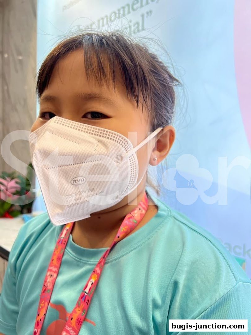 A young person wearing a mask and a turquoise t-shirt with a colorful lanyard.